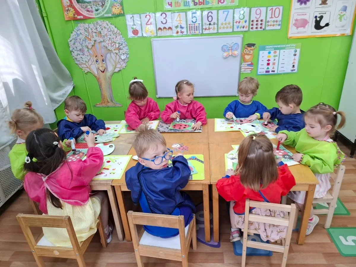 Дети в фартуках занимаются творчеством за большим столом